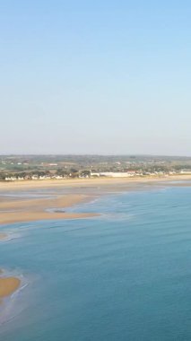 Grande Plage de Barneville 'deki kumlu sahil manzarası ve sakin mavi sular. Sahil boyunca uzanan uzak evler berrak bir gökyüzü altında..