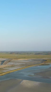 Fransa 'nın açık mavi gökyüzünün altında Le Mont-Saint-Michel yakınlarındaki araziye uzanan gelgit düzlüklerinin ve eğimli bir geçitin havadan görünüşü.