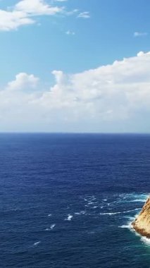 Derin mavi okyanus, Fanale di Petra yakınlarında bulutlu bir gökyüzünün altında engebeli bir kayalık kıyı şeridiyle buluşuyor. Doğal güzellik ve berrak su ile sakin deniz manzarası.