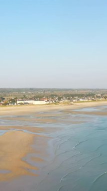 Geniş kumlu sahil, hafif dalgalar ve berrak mavi gökyüzünün altındaki Barneville-Carteret köyü manzarası. Fransa, Normandiya 'da sakin kıyı manzarası.