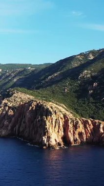 Korsika 'daki Porto Vadisi' nde berrak bir gökyüzünün altında dramatik kayalık kayalıklar yükseliyor. Bereketli yeşil tepeler engebeli kıyı manzarasını çerçeveliyor..