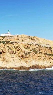 Fanale di Petra 'nın engebeli kayalık kıyı şeridine tünemiş deniz fenerinin manzarası. Derin mavi deniz ve berrak gökyüzü. Seyahat ve deniz teması için doğal manzara ideal.