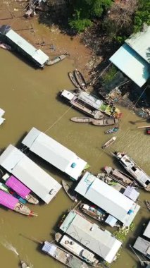 Vietnam 'daki Cai Rang yüzer pazarında, nehir kenarındaki binalar ve ağaçlar çamurlu su boyunca görülebilen ağaçlarla birlikte teknelerin tepeden aşağı insansız hava aracı görüntüleri..