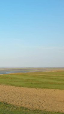 Fransa 'nın Le Mont-Saint-Michel yakınlarındaki açık mavi gökyüzünün altındaki çimenli tarlaların ve gelgit düzlüklerinin geniş bir görüntüsü. Huzurlu doğal manzara arka plan veya seyahat kavramları için idealdir.