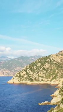Korsika 'daki Calanques de Piana kıyı şeridi boyunca uzanan engebeli uçurumların manzarası berrak mavi bir gökyüzünün altında.