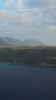 Yunanistan 'ın Mani bölgesinde Diros plajı yakınlarında bulutlu bir gökyüzü altında yuvarlanan yeşil tepelerin ve derin mavi denizin manzarası.