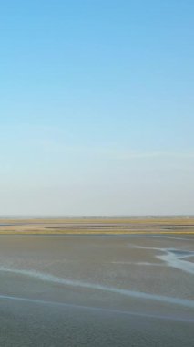 Fransa 'nın Le Mont-Saint-Michel şehrinde açık mavi gökyüzünün altında gelgit düzlükleri ve sığ su manzarası geniş. Doğal dokuları ve yumuşak ışıklarıyla huzurlu bir manzara..