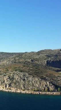 Yunanistan 'ın Nafplio kentinde açık mavi bir gökyüzünün altında kıyı şeridi boyunca uzanan kayalık bir kıyı yamacının geniş manzarası.