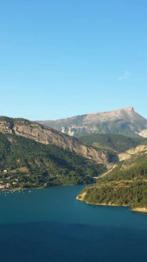 Turkuaz sularla kaplı, ormanlık tepeleri çevreleyen Castillon Gölü 'nün ve berrak mavi gökyüzünün altındaki uzak bir dağın manzarası..