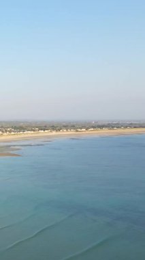 Geniş kumlu kıyı şeridi ve sakin mavi sular Grande Plage de Barneville, Normandiya, Fransa 'da, açık bir gökyüzü altında kıyı boyunca uzanan uzak evler..