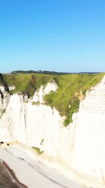Üzerinde yeşil çimenler ve altında dar bir plaj bulunan dramatik beyaz tebeşir kayalıkları Etretat, Normandiya, Fransa 'da açık mavi bir gökyüzünün altında.