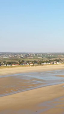 Grande Plage de Barneville, Normandiya 'da, açık mavi gökyüzünün altında gelgit havuzları ve uzak evleri olan geniş kumlu sahil..