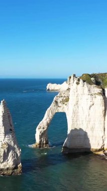 Dramatik beyaz tebeşir kayalıkları ve açık bir gökyüzünün altında Etretat, Normandiya 'da mavi denizin üzerinde yükselen doğal bir taş kemer. Çarpıcı kaya oluşumlarıyla ikonik kıyı manzarası.