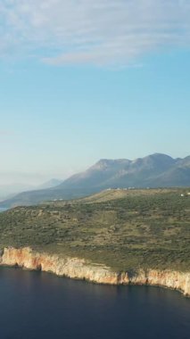 Yunanistan 'ın Mani bölgesindeki Diros plajı yakınlarındaki açık bir gökyüzü altında sarp kayalıkları ve uzak dağları olan engebeli kıyı şeridi manzarası.