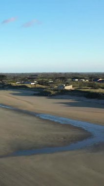 Narin kum tepeleri ve dağınık binaları olan geniş kumlu bir sahil. Utah Beach, Normandiya 'da açık mavi bir gökyüzünün altında yeşil kırsalla çevrili..