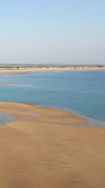 Geniş kumlu sahil ve Grande Plage de Barneville, Normandiya, Fransa 'da berrak bir gökyüzünün altında sakin mavi deniz. Kıyı evleri uzaktan görülebilir..