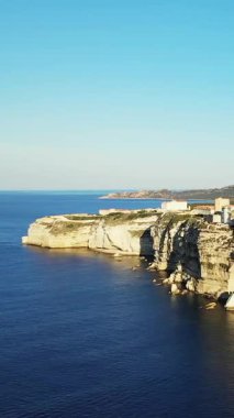 Korsika 'nın Bonifacio kıyı şeridi boyunca berrak beyaz kireçtaşı kayalıkları ve berrak mavi deniz manzarası. Güneş ışığı dramatik manzarayı ve kıyı mimarisini vurguluyor..