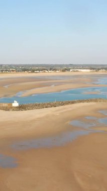Fransa 'nın Normandiya eyaletindeki Grande Plage de Barneville' de gel-git havuzları ve taştan dalgalı suyu olan geniş kumlu bir sahil. Berrak gökyüzü altında sakin kıyı manzarası.