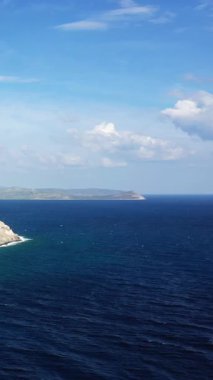 Derin mavi deniz manzarası ve Yunanistan 'ın Monemvasia kenti yakınlarında parlak bir gökyüzünün altındaki uzak kıyı şeridi. Dağılmış bulutlar ve açık ufuk ile sakin deniz manzarası.
