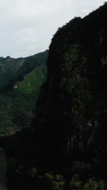 Nong Khiaw, Laos 'ta bulutlu bir gökyüzünün altındaki sarp, ormanlı dağların dramatik manzarası. Yoğun yeşillik engebeli kayalıkları kaplayarak çarpıcı bir doğal manzara yaratıyor..