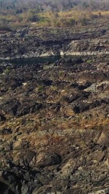 Gün doğumunda Laos 'taki Tat Somphamit Şelaleleri' ndeki kayalık nehir yatağının geniş manzarası. Nadir bitki örtüsü ve açık kayalar dramatik bir doğal manzara yaratır..