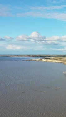 Parlak mavi bir gökyüzü ve dağınık bulutlar altında sakin bir nehir veya haliçlerin geniş bir görüntüsü. Açık kırsallı doğal, sakin bir su manzarası..