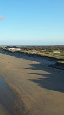 Geniş kumlu sahil şeridi, yumuşak kum tepeleri ve Utah Sahili, Normandiya 'da açık mavi gökyüzü. Uzak binalar ve yeşilliklerle sakin kıyı manzarası.