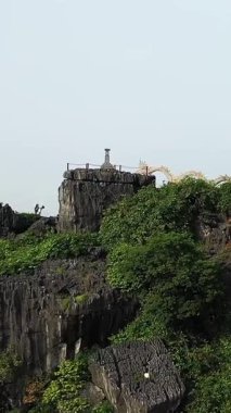 Hang Mua 'nın Vietnam, Ninh Binh' deki manzarası. Kayalık kayalıkların tepesindeki kaya heykeli yemyeşil tarlalara ve uzak kireçtaşı dağlarına bakıyor..