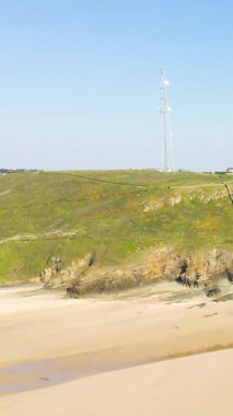 Geniş kumlu sahil ve yüksek bir iletişim kulesi olan kayalık uçurumlar Fransa 'nın Cap de Carteret kentindeki çimenli bir tepede açık mavi gökyüzünün altında..