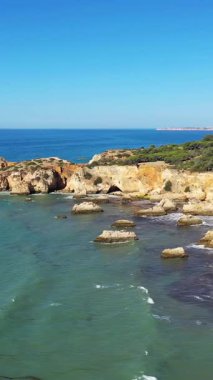 Albufeira yakınlarındaki engebeli Algarve sahil şeridinin turkuaz suları ve berrak mavi gökyüzünün altındaki dramatik uçurumları manzarası..