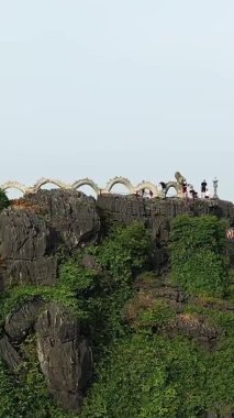 Hang Mua bakış açısı Ninh Binh, Vietnam 'da, kayalık kayalıkların tepesindeki sarmal ejderha heykeli, yemyeşil pirinç tarlalarına ve uzak şehir manzarasına bakıyor..