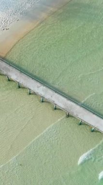 Coconut Sahili 'ndeki turkuaz suyu boyunca uzanan beton iskelenin insansız hava aracı görüntüsü. Hafif dalgalar ve kumlu kıyı şeridi görülebiliyor..