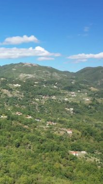 Scenic aerial view of rolling green hills and scattered rural houses under a clear blue sky in Fiumicello, Italy.