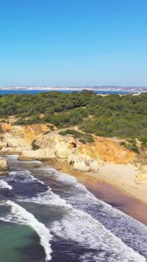 Portekiz 'in Albufeira yakınlarındaki Algarve kıyı şeridi boyunca açık mavi gökyüzü altında dramatik uçurumlar, yemyeşil dalgalar manzaralı..