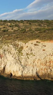 Yunanistan 'ın Mani bölgesindeki Diros Sahili' nin yanındaki mavi denizin üzerinde parçalı bulutlu bir gökyüzünün altında yükselen sarp kayalıklar..