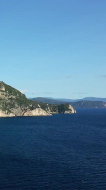 Yunanistan 'ın Parga kenti yakınlarında açık bir gökyüzünün altında derin mavi denizle buluşan engebeli yeşil uçurumların manzarası. Huzurlu Akdeniz manzarası seyahat ve doğa kavramları için ideal.