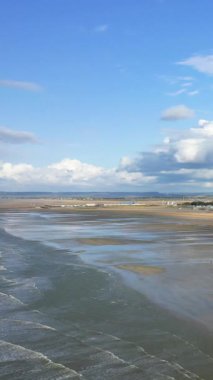 Lion-sur-Mer, Normandiya 'da Sword Beach' in geniş bir manzarası var. Islak kum, mavi gökyüzünü ve dağınık bulutları yansıtıyor..