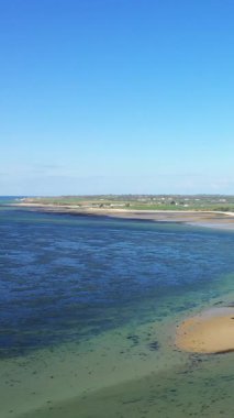 Fransa, Grandcamp-Maisy 'deki kumlu sahil ve sahil manzaralı açık mavi bir gökyüzünün altında. Sakin sular ve uzak kırsal alanlar huzurlu bir sahil manzarası yaratır..