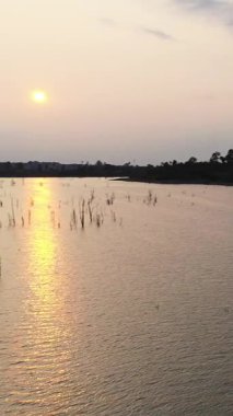 Gün batımında Nakai gölünün sakin suları gölden yükselen siluetli ağaç kütükleri ve yumuşak pastel bir gökyüzünün altındaki uzak tepeler..