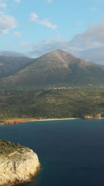 Yunanistan 'ın Mani bölgesindeki Diros Sahili yakınlarında, yemyeşil bir yeşilliğin üzerinde yükselen bir dağın manzarası ve bulutlu bir gökyüzünün altında sakin bir kıyı şeridi..