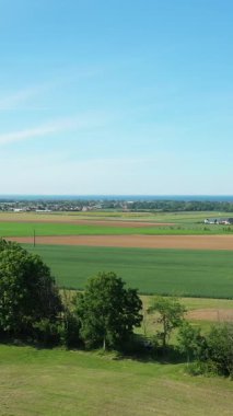 Fransa 'nın Hillman kenti yakınlarındaki açık mavi gökyüzünün altında yeşil tarlalar, tarım arazileri ve uzak köyün havadan görünüşü. Bereketli bitki örtüsü ve açık alanlı huzurlu kırsal manzara.