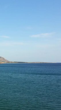 Yunanistan 'ın Analipsi kentinde uzak kıyı şeridi ve açık gökyüzü ile sakin mavi deniz. Huzurlu sular ve doğal manzara huzurlu bir sahil manzarası yaratır..