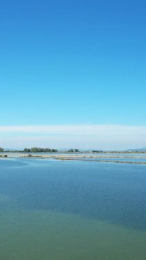 Yunanistan 'ın Missolonghi kentinde açık mavi bir gökyüzü altında sakin tuz bataklıkları geniş bir görünüm. Sakin su ve uzak toprak sakin bir doğal manzara yaratır..