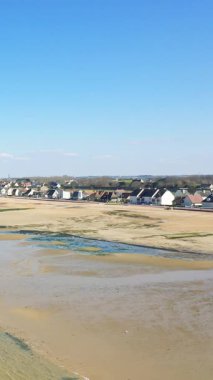Bernieres-sur-Mer, Normandiya 'da açık mavi gökyüzünün altında kıyı evleri olan geniş kumlu bir sahil. Dalgalar, kıyı şeridi boyunca ıslak kum ve gelgit havuzlarını ortaya çıkarır..