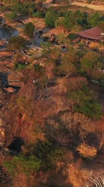 Tat Somphamit Li Phi şelalelerinin Laos 'ta gün batımında kayalık arazi ve yemyeşil ağaçlarla çevrili hava manzarası. Akan su ve doğal güzellikle dramatik bir manzara..