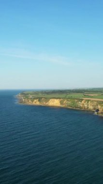 Normandiya, Fransa 'da açık mavi gökyüzü ve sakin denizle dramatik uçurumlar ve kıyı şeridi. Engebeli arazi ve yeşil tarlalar okyanusla buluşuyor..