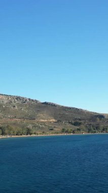 Açık mavi su ve Yunanistan 'ın Nauplie kenti yakınlarındaki Paralia Karathona sahilinde parlak bir gökyüzünün altında kayalık bir yamaç. Huzurlu doğal manzara seyahat ve rahatlama temaları için ideal.