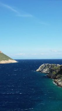 Yunanistan 'ın Porto Kagio kenti yakınlarında parlak bir gökyüzü altında kayalık kıyı şeridi ve berrak mavi denizin manzarası. Manzarada engebeli uçurumlar ve canlı turkuaz suları yer alıyor..