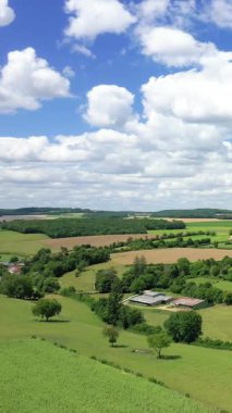 Bereketli yeşil tarlalar, tarım arazileri ve Fransız kırsalında kabarık bulutları olan açık mavi gökyüzünün altındaki dağınık ağaçlar..