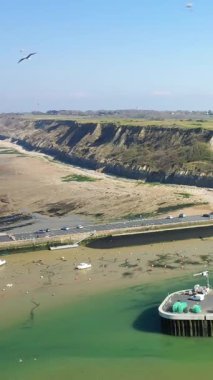 Açık bir günde Fransa 'nın Normandiya eyaletinin Port en Bessin kentindeki liman ve dramatik sahil uçurumlarının hava manzarası. Sahnede turkuaz su, tekne ve engebeli bir kıyı şeridi yer alıyor..